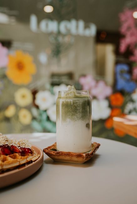 A cozy table setting with a matcha latte and waffle in a floral-decorated cafe.