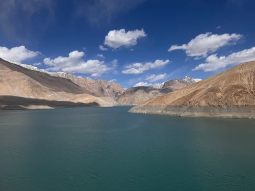 Free Stunning view of a tranquil lake surrounded by towering mountains under a blue sky with fluffy clouds. Stock Photo