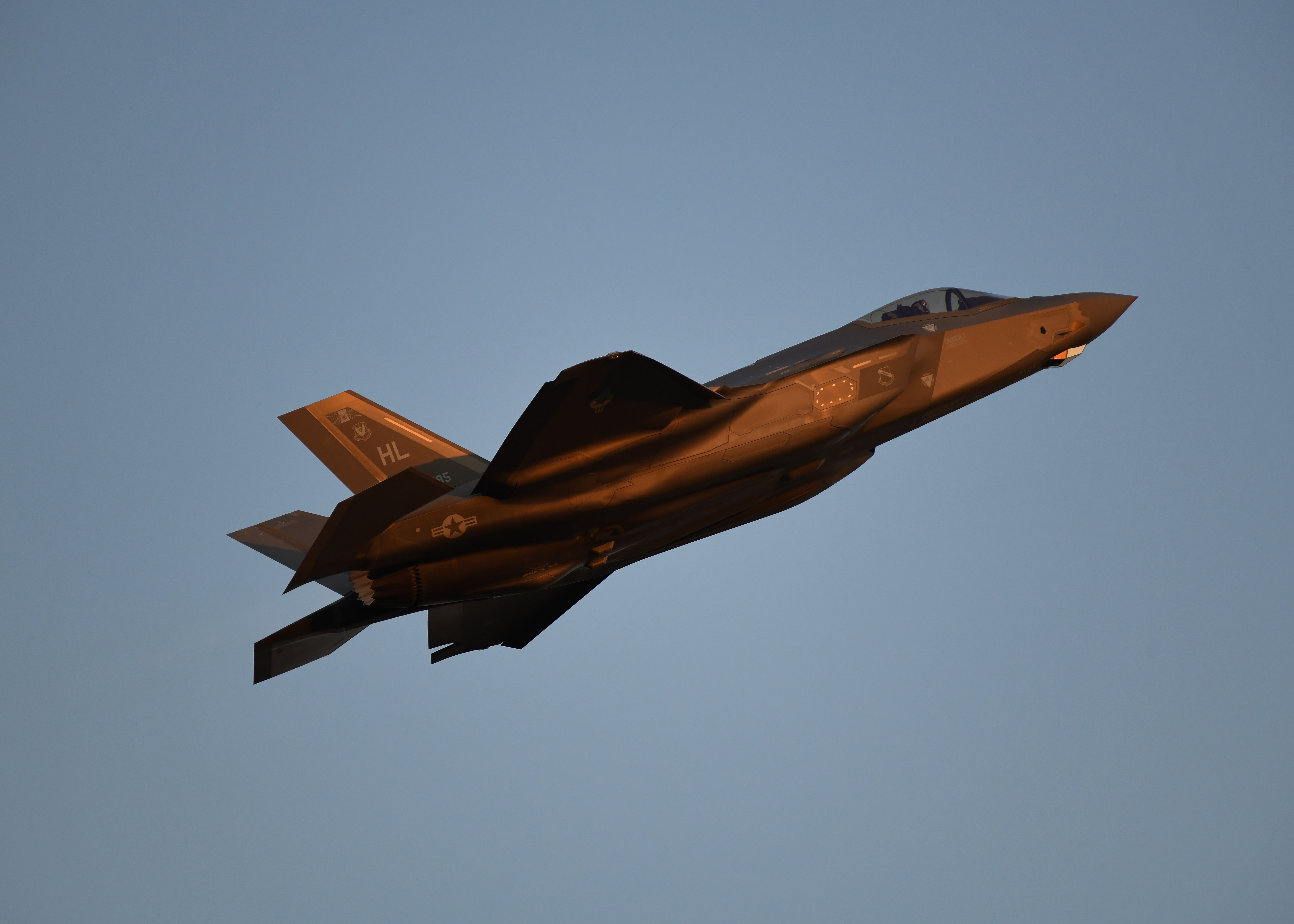 Een F-35 gevechtsvliegtuig in volle vlucht, vastgelegd tegen een heldere hemel bij zonsondergang.
