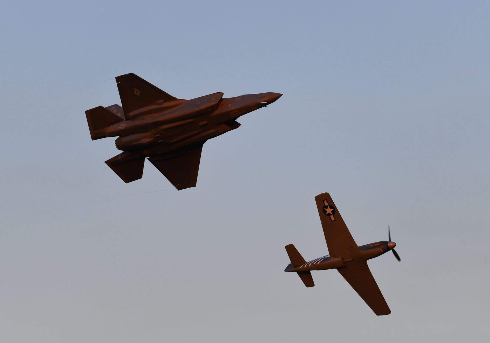Two fighter jets perform an aerial maneuver against a clear evening sky.