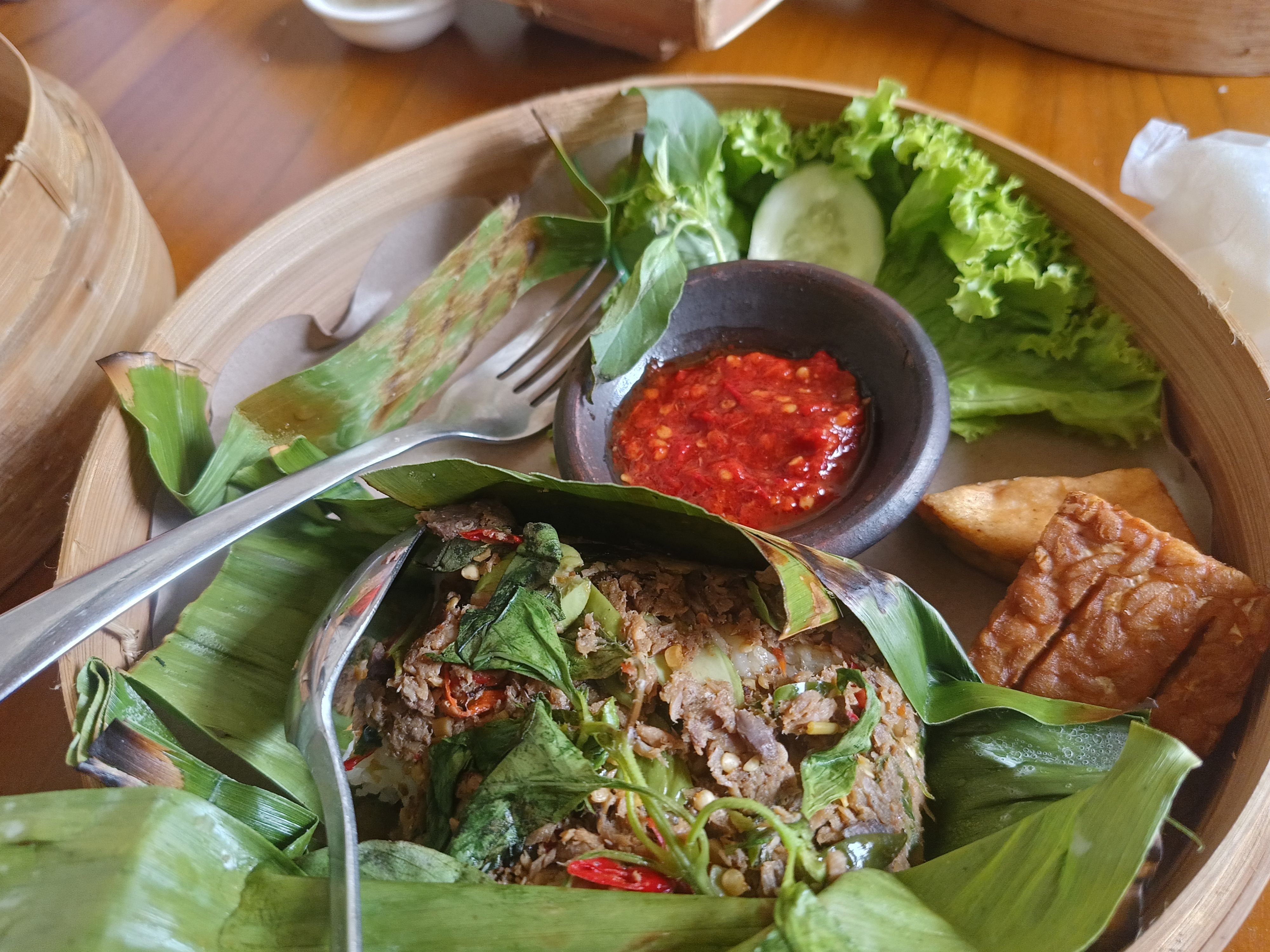 A traditional Indonesian dish wrapped in banana leaf with spicy sambal, tofu, tempeh, and fresh salad.