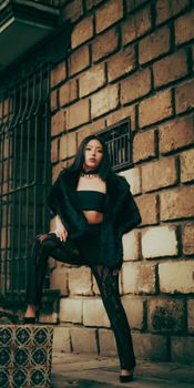 Stylish woman in black outfit posing confidently against a rustic brick wall. Urban fashion and attitude.