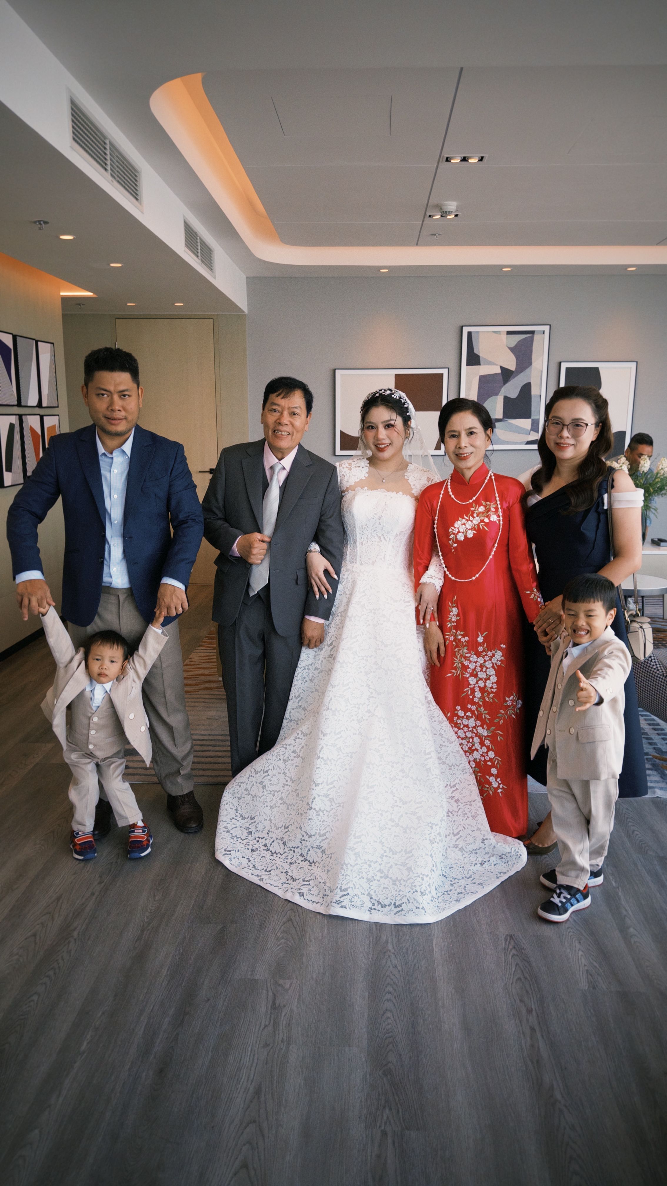 A joyful Vietnamese family wedding portrait featuring the bride in a white dress and family in traditional attire.