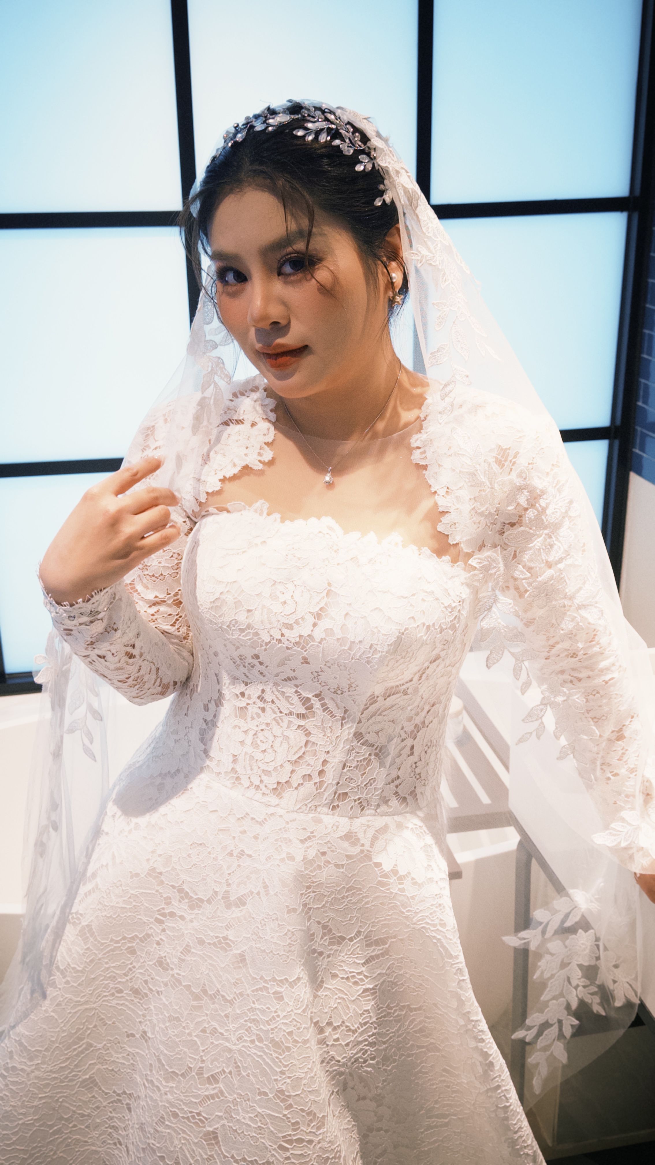 Beautiful Asian bride wearing a lace wedding dress indoors on her special day.