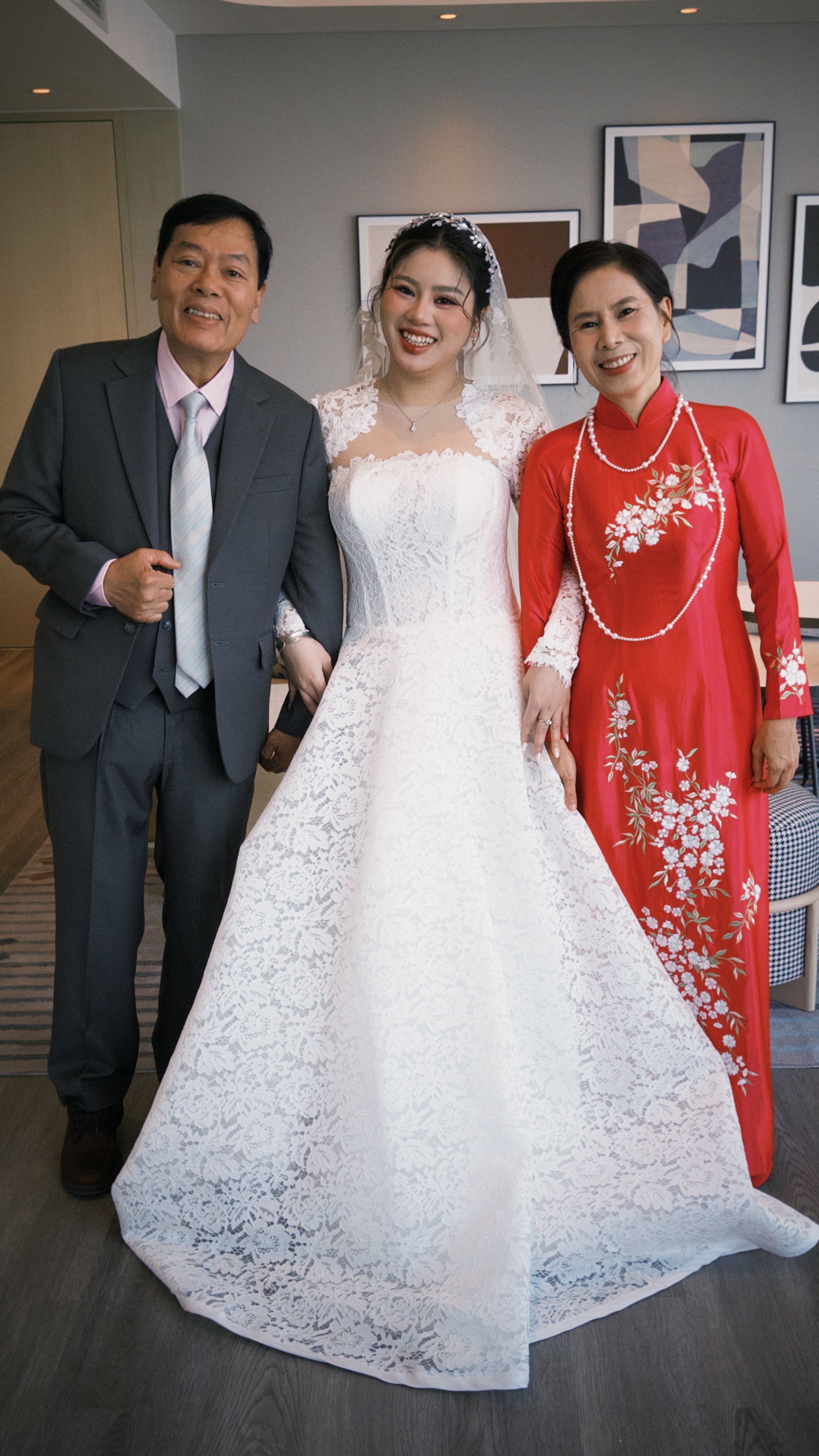 Bride in white gown with parents in traditional Vietnamese attire celebrating indoors.