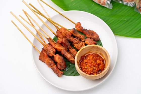 Charred pork satay skewers on banana leaf with a wooden bowl of red chili sambal