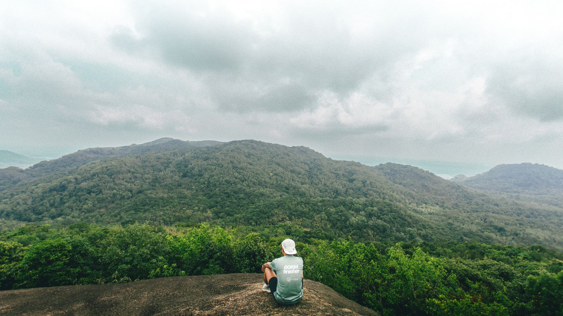Man observes vast green mountains from a rocky vantage in Ho Chi Minh City, Vietnam.