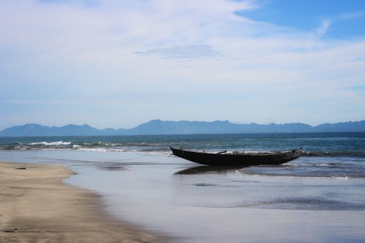 Tranquil beach scene in Bangladesh featuring an empty boat at the sea shore under a blue sky.
