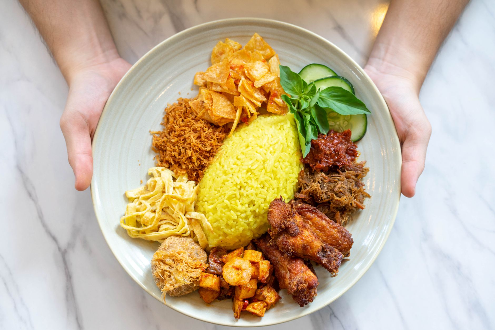 A vibrant Nasi Kuning plate with traditional Indonesian sides served on a marble table.