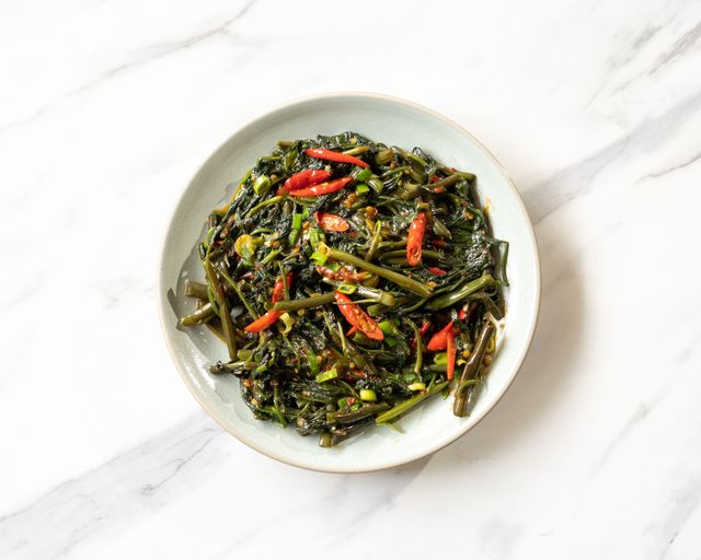 A flavorful and spicy Plecing Kangkung dish, a traditional Balinese delicacy served on a white plate.