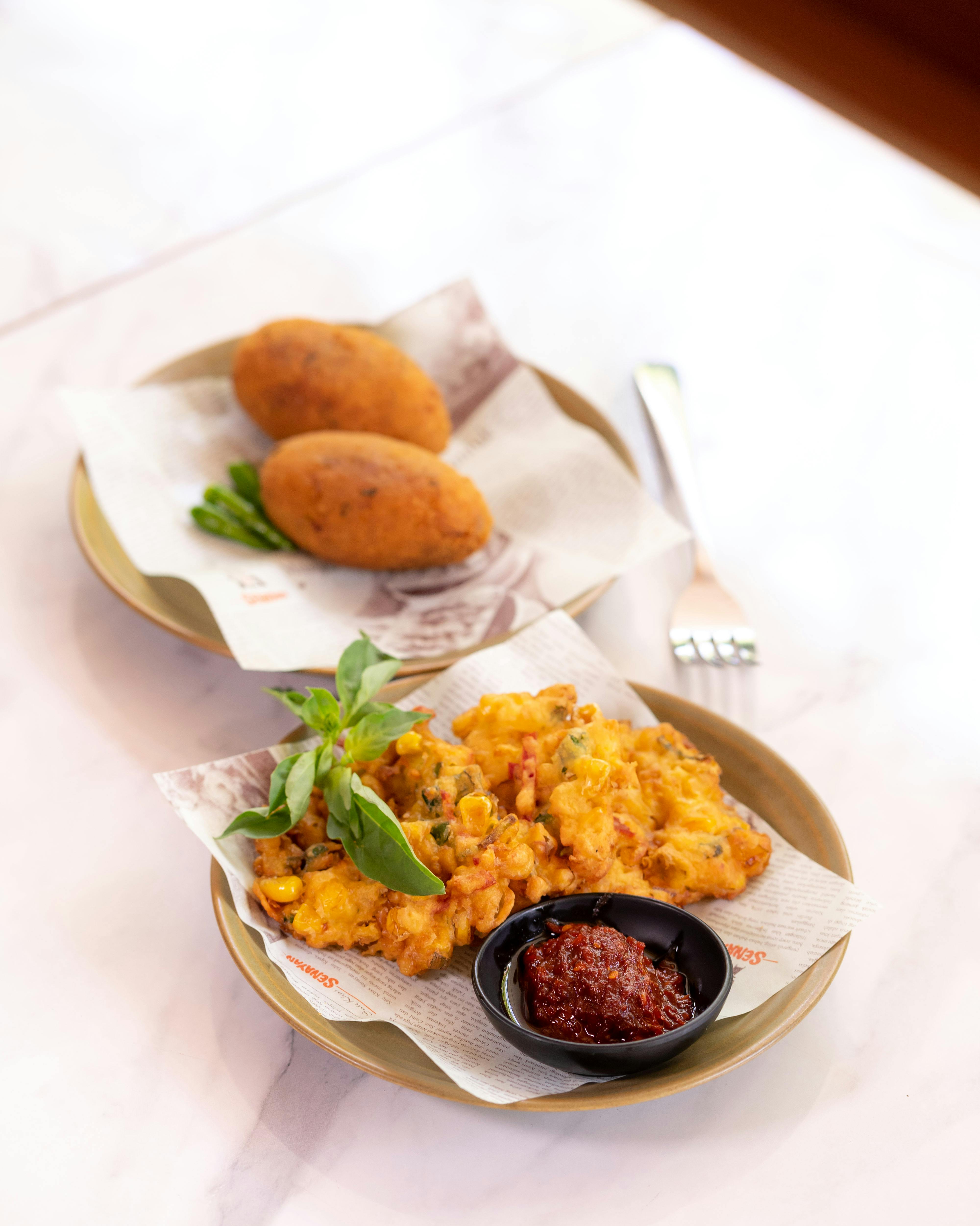 Bakwan jagung renyah dengan sambal dan daun segar di piring