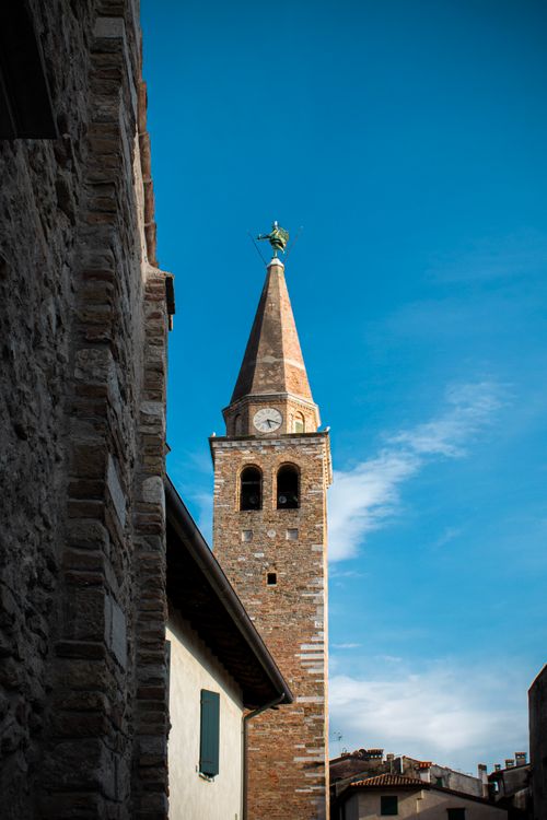 Free A stunning view of a historic church tower in Grado, Italy, under a clear blue sky. Stock Photo
