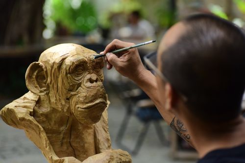 Free Artisan carving intricate details on a wooden chimpanzee sculpture outdoors. Stock Photo