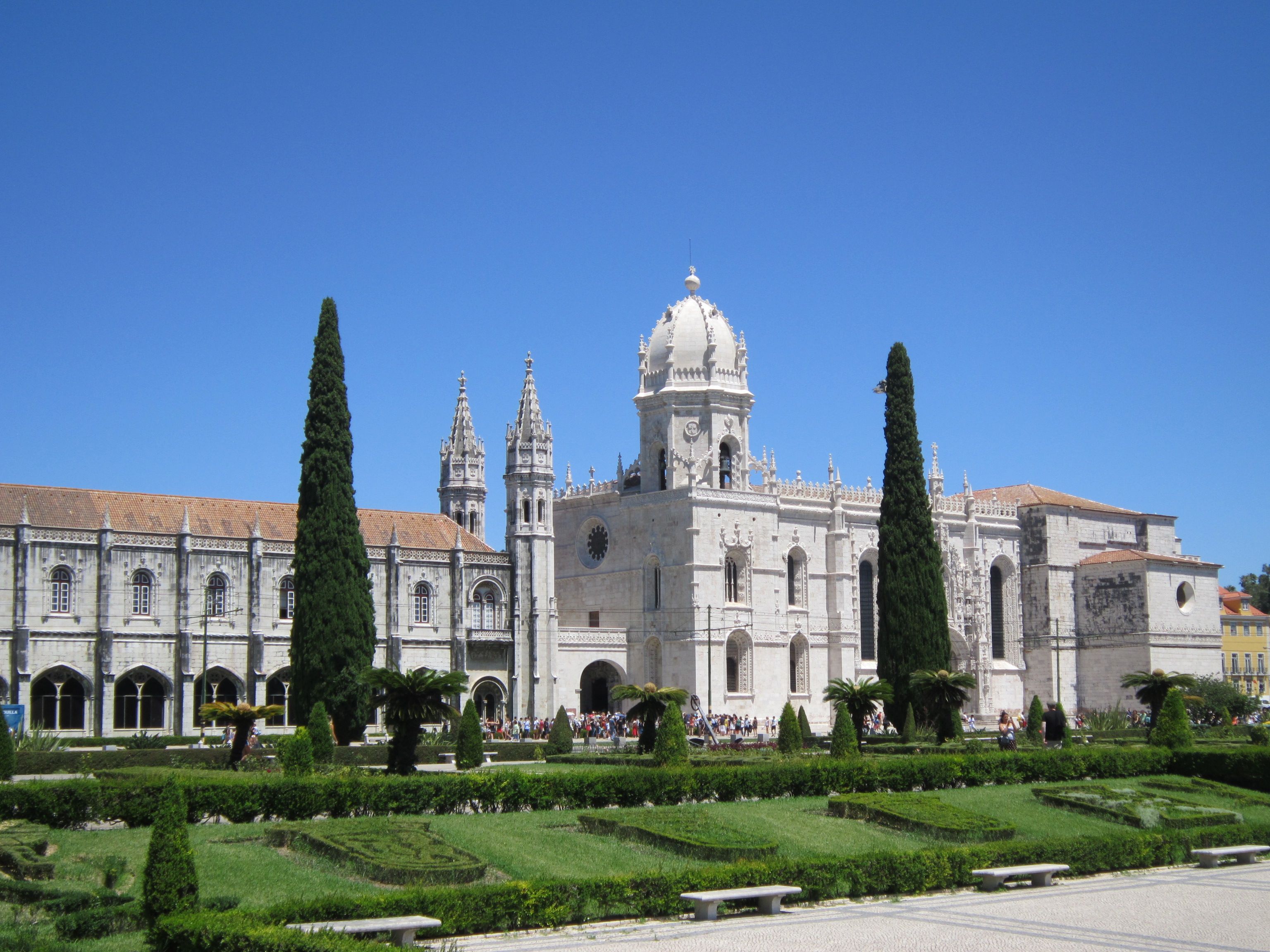 A captivating view of Jeronimos Monastery in Lisbon, Portugal with lush greenery and a bright blue sky.