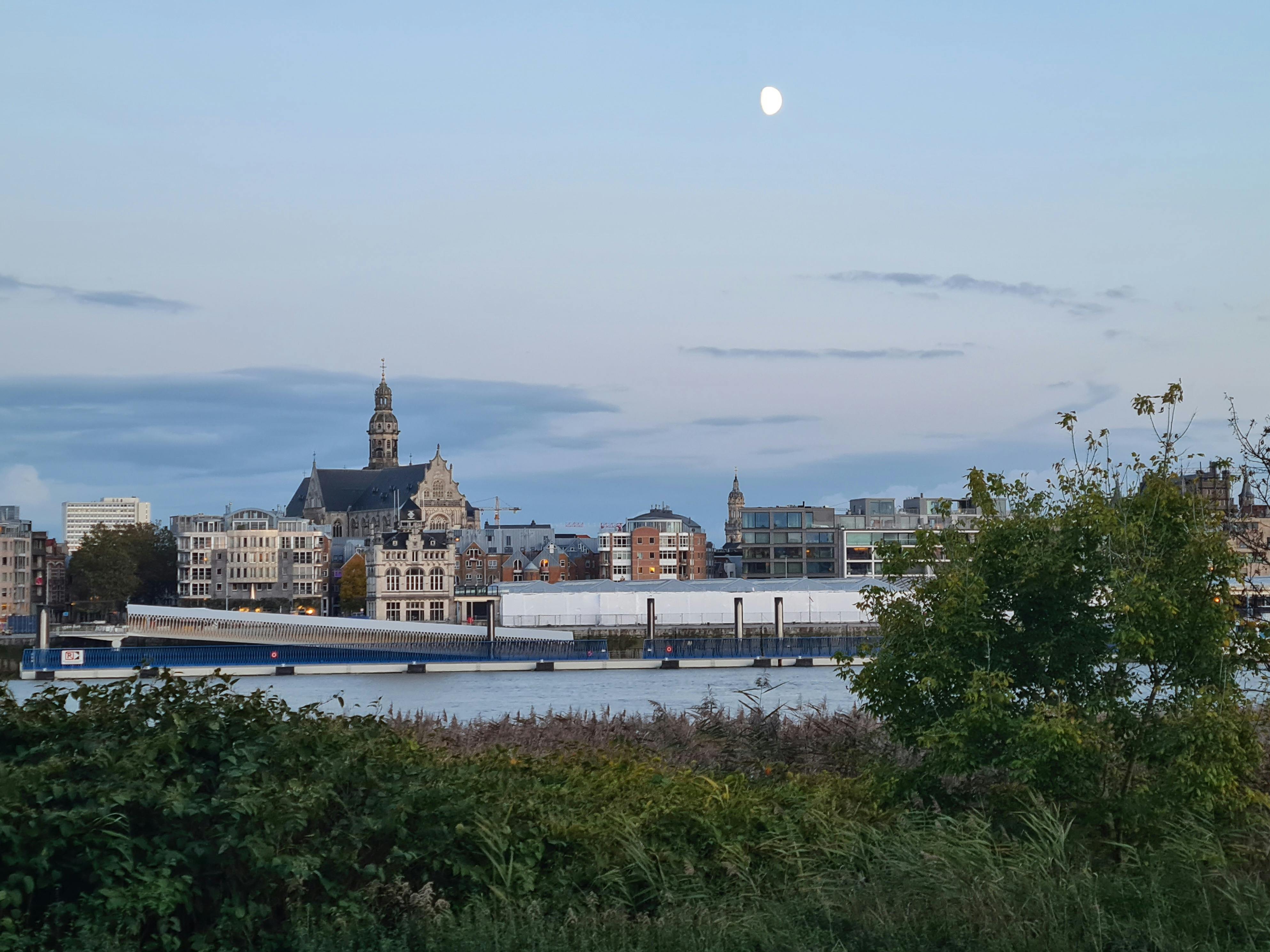 Scenic view of Antwerp's cathedral and skyline at twilight with moon overhead.