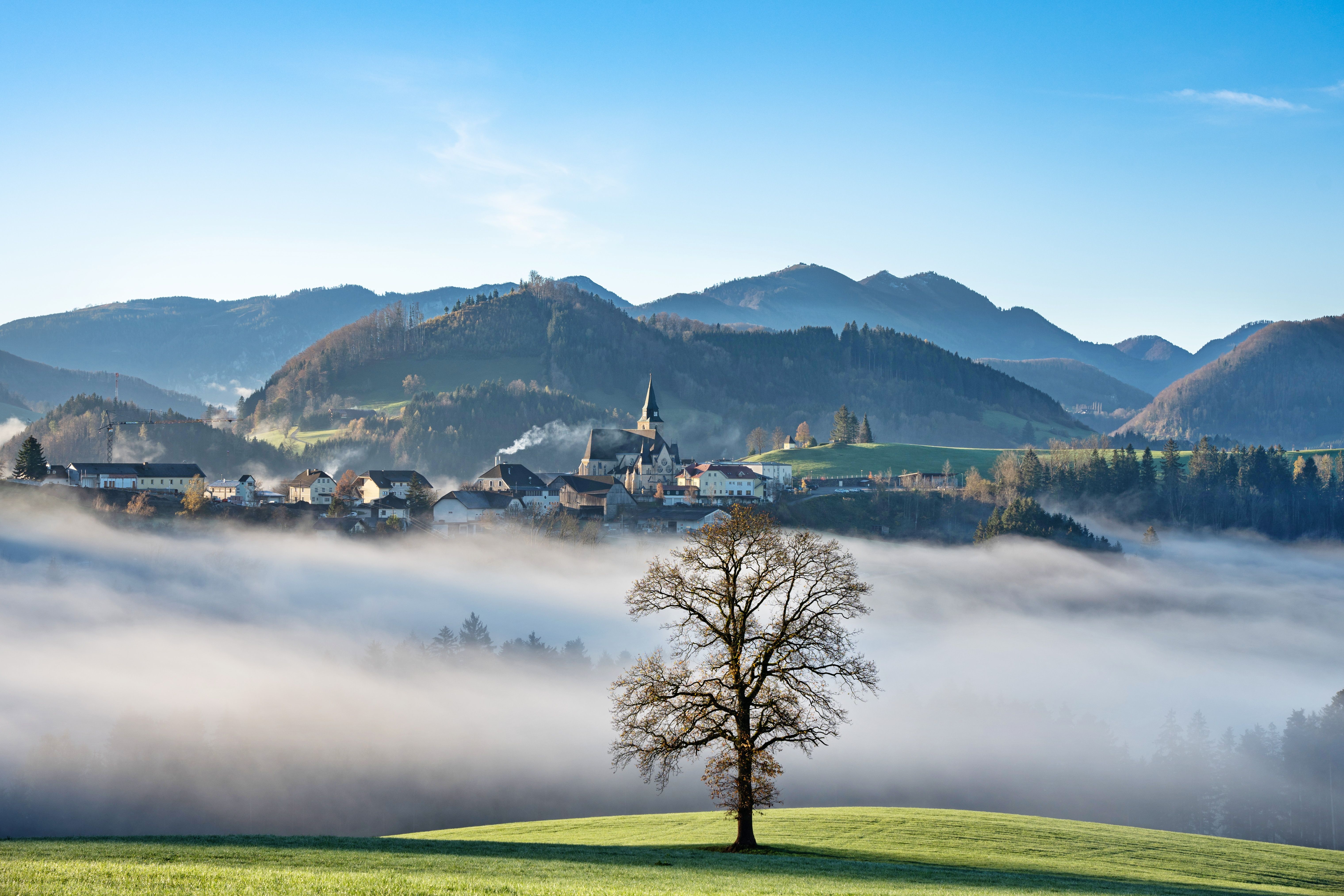 A picturesque view of Maria Neustift village surrounded by fog and mountains in the morning sun.