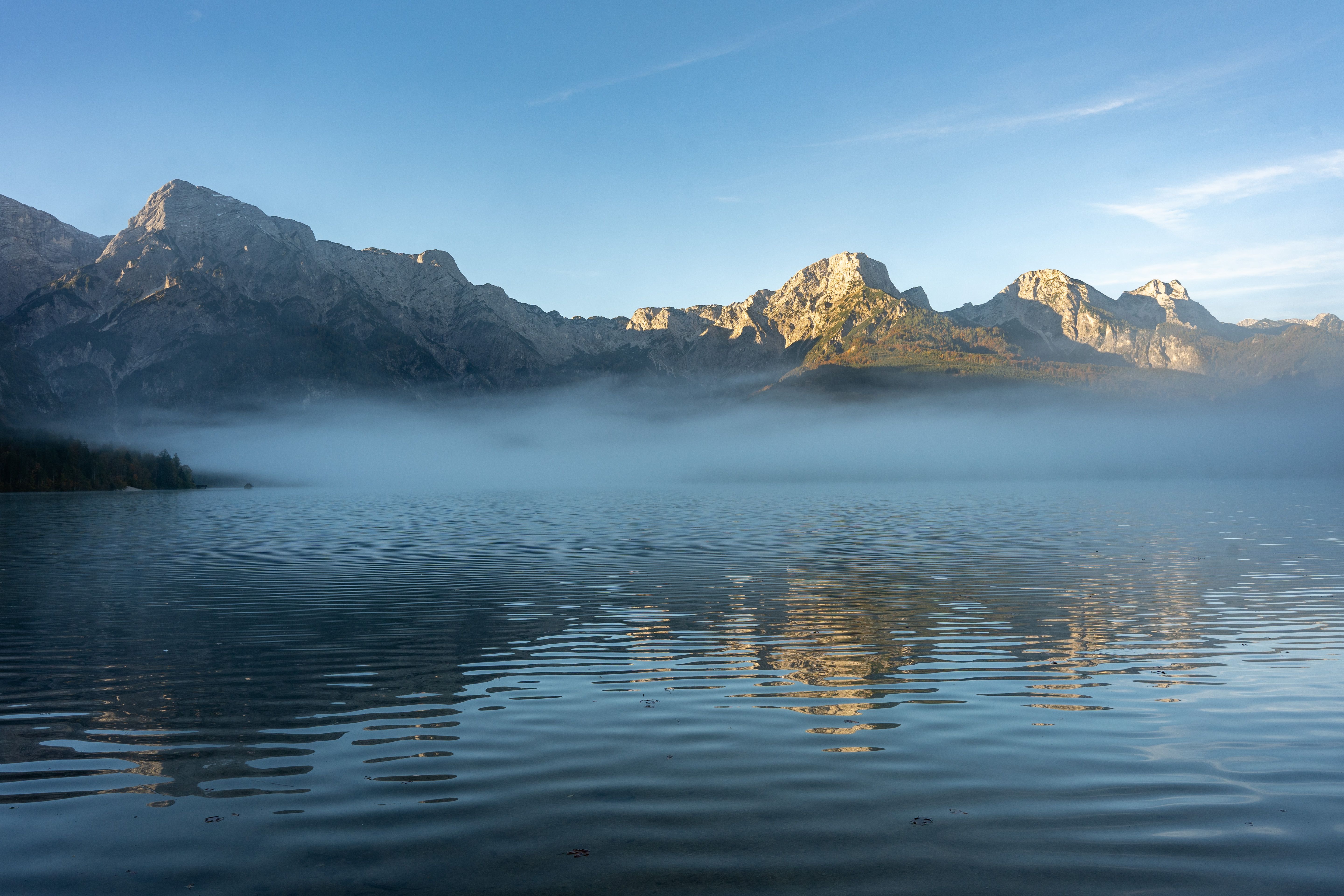Serene misty lake with reflections of Alpine mountains at sunrise in Oberösterreich, Austria.