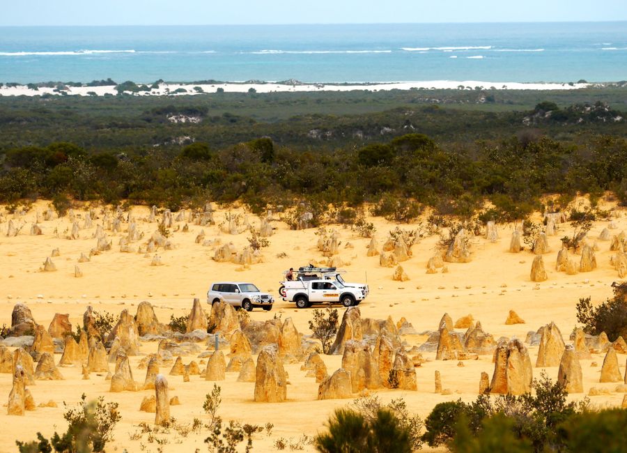 Scenic view of vehicles in the Pinnacles Desert, Western Australia, with ocean in the background.