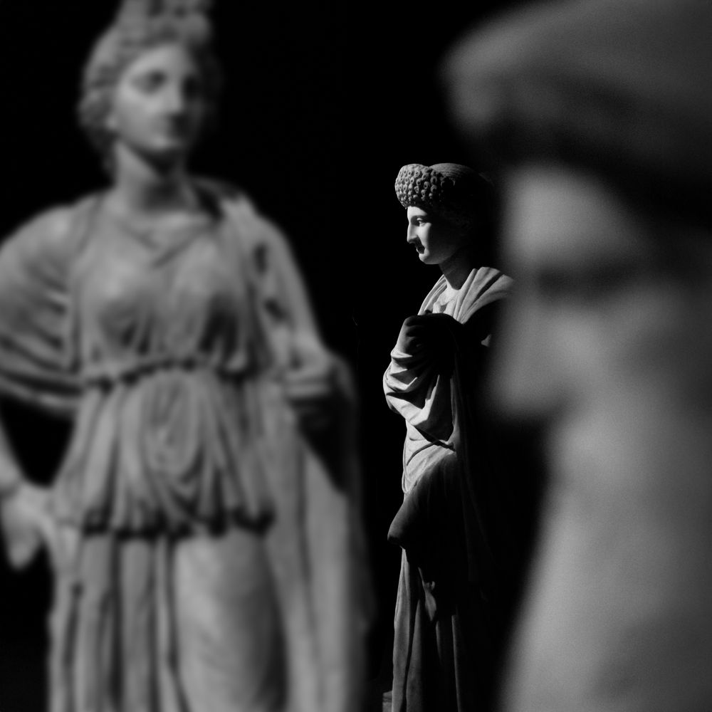Classical marble statues of draped women in the dim light of a museum gallery.
