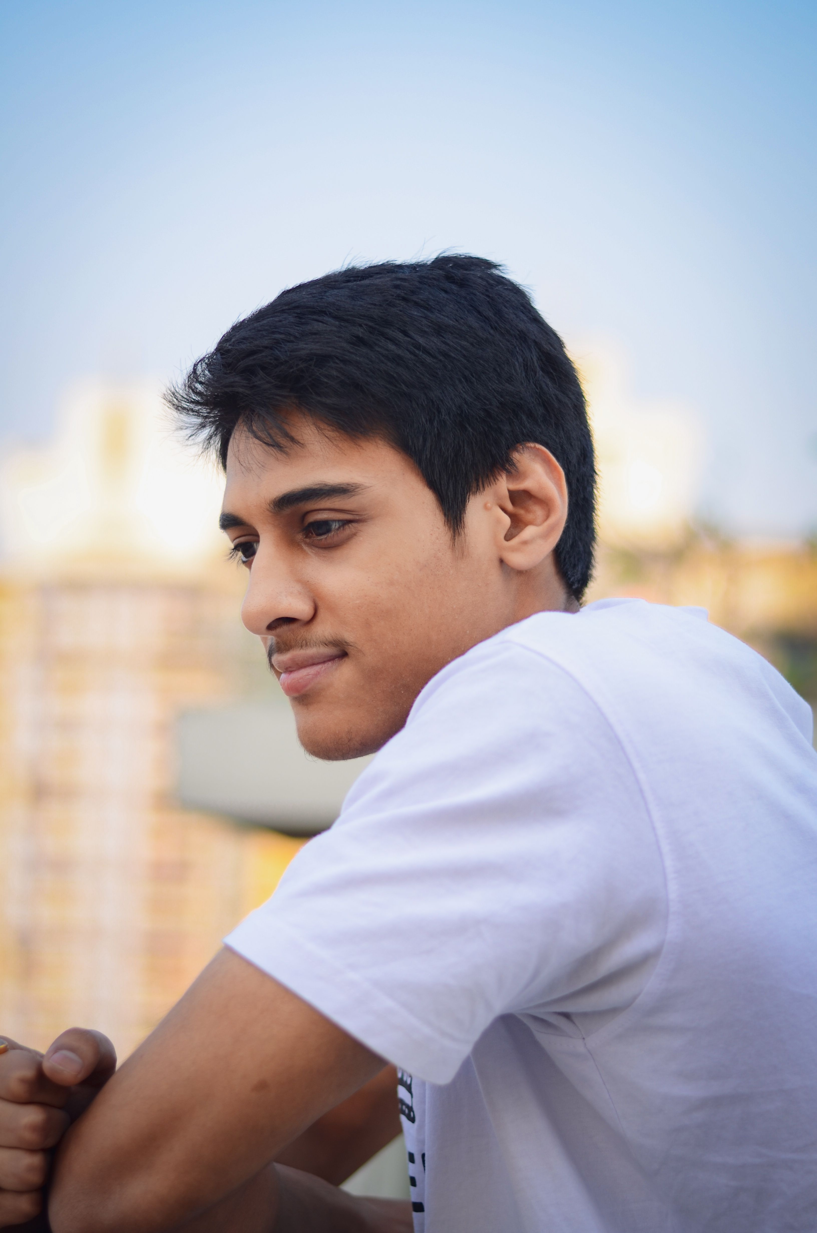 A young man in a white T-shirt gazes thoughtfully while leaning on a railing outdoors in Kolkata.