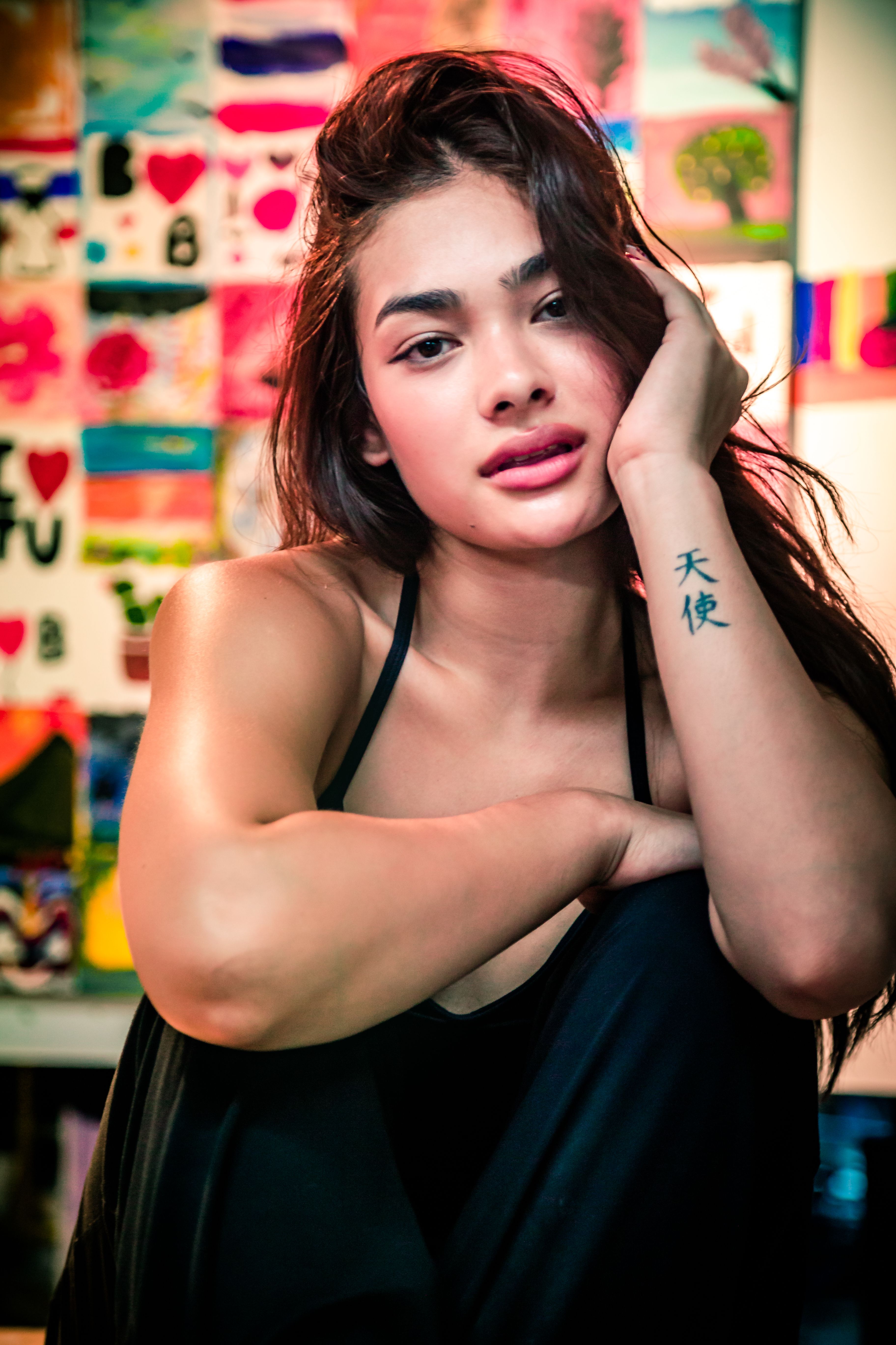 Close-up of a young woman with a tattoo, surrounded by colorful artwork.