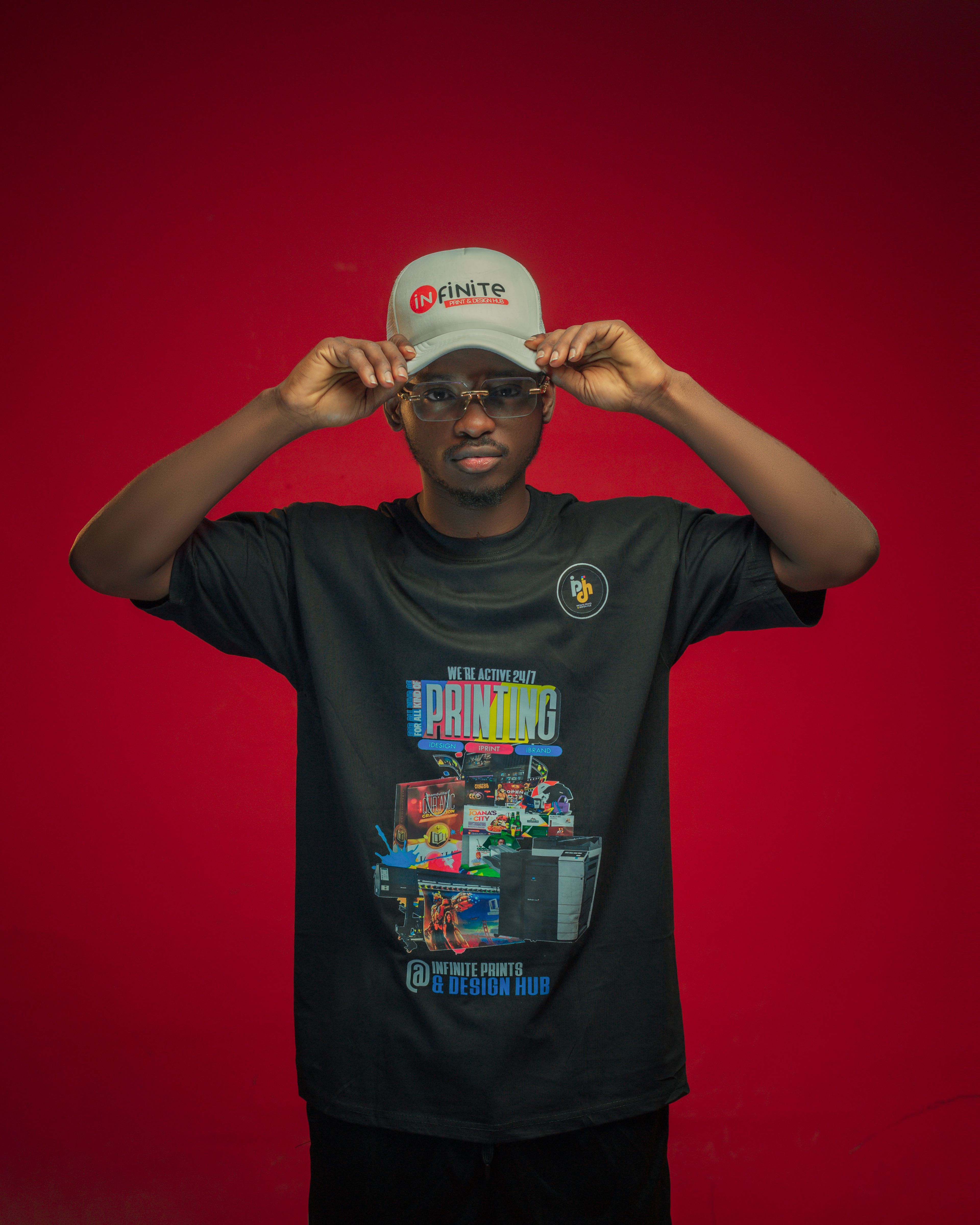 Young man adjusting his cap, standing against a vibrant red backdrop, embodying modern fashion.