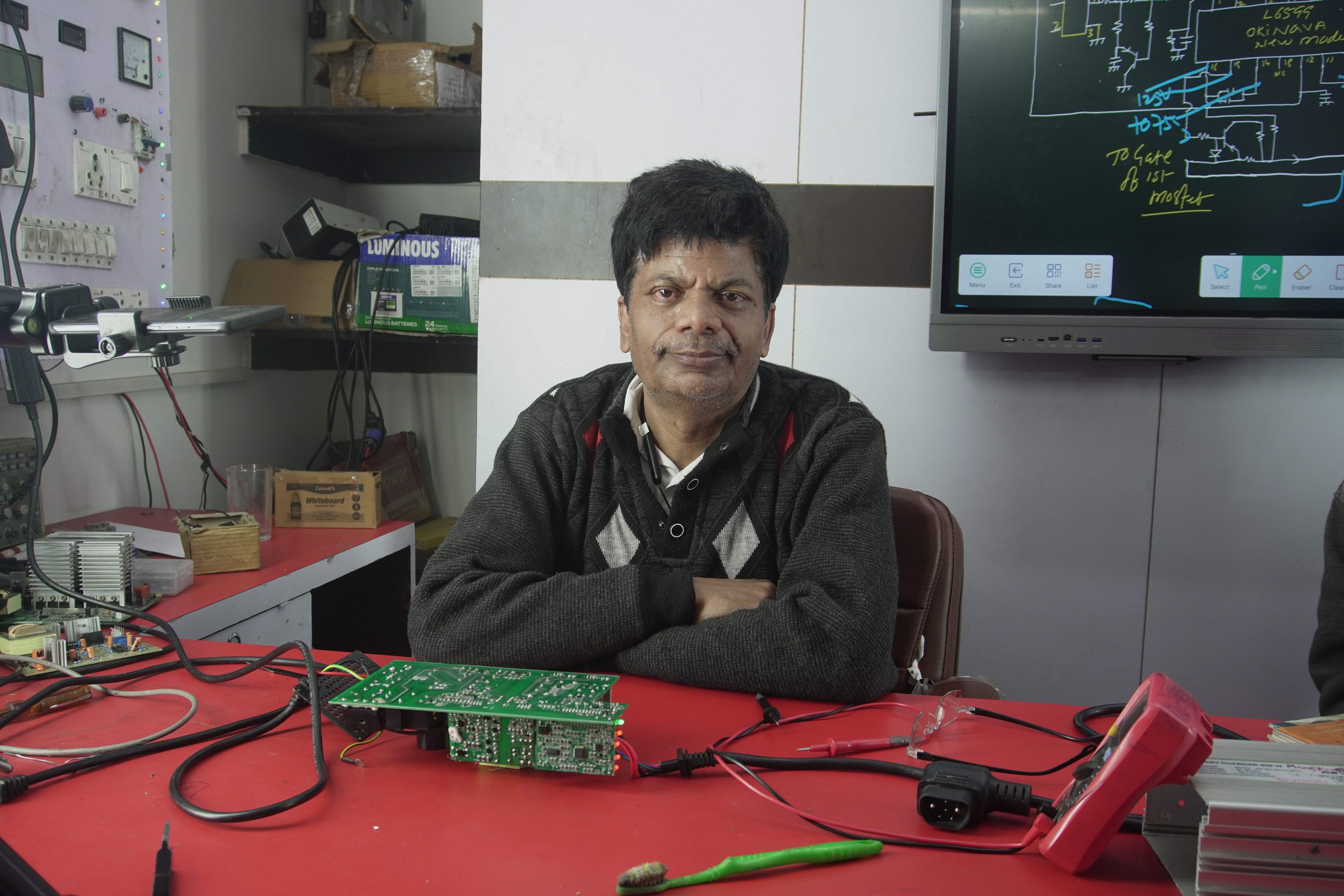 An electronics engineer works at the repair lab desk, surrounded by tools and a circuit board.
