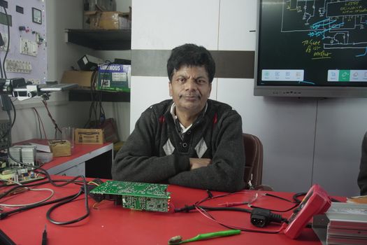 An electronics engineer works at the repair lab desk, surrounded by tools and a circuit board.