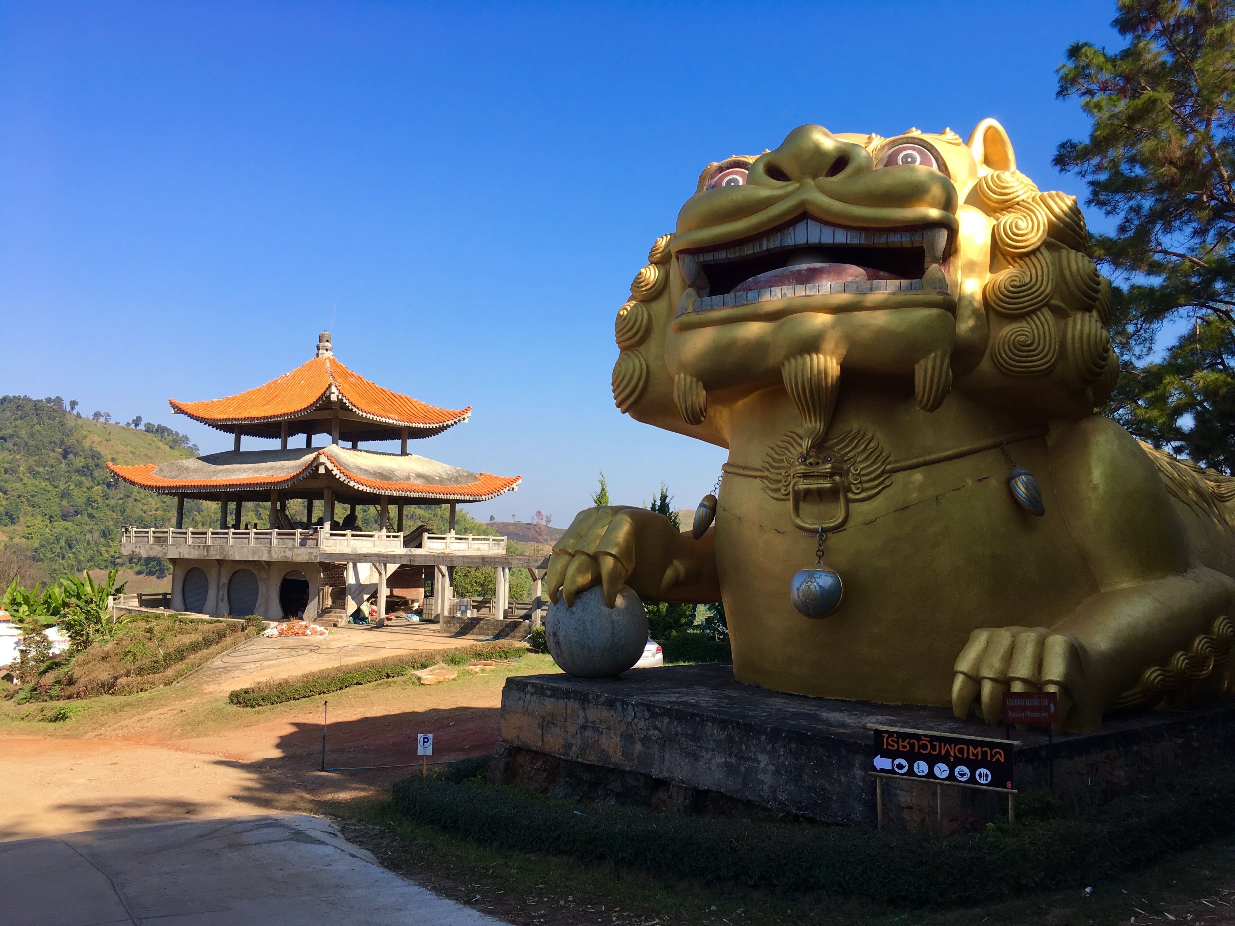 Golden guardian statue and traditional Thai temple under clear blue sky in Thailand.