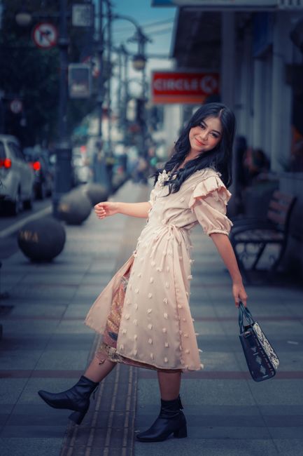 Chic woman in pink dress poses on urban street in Bandung, Indonesia.