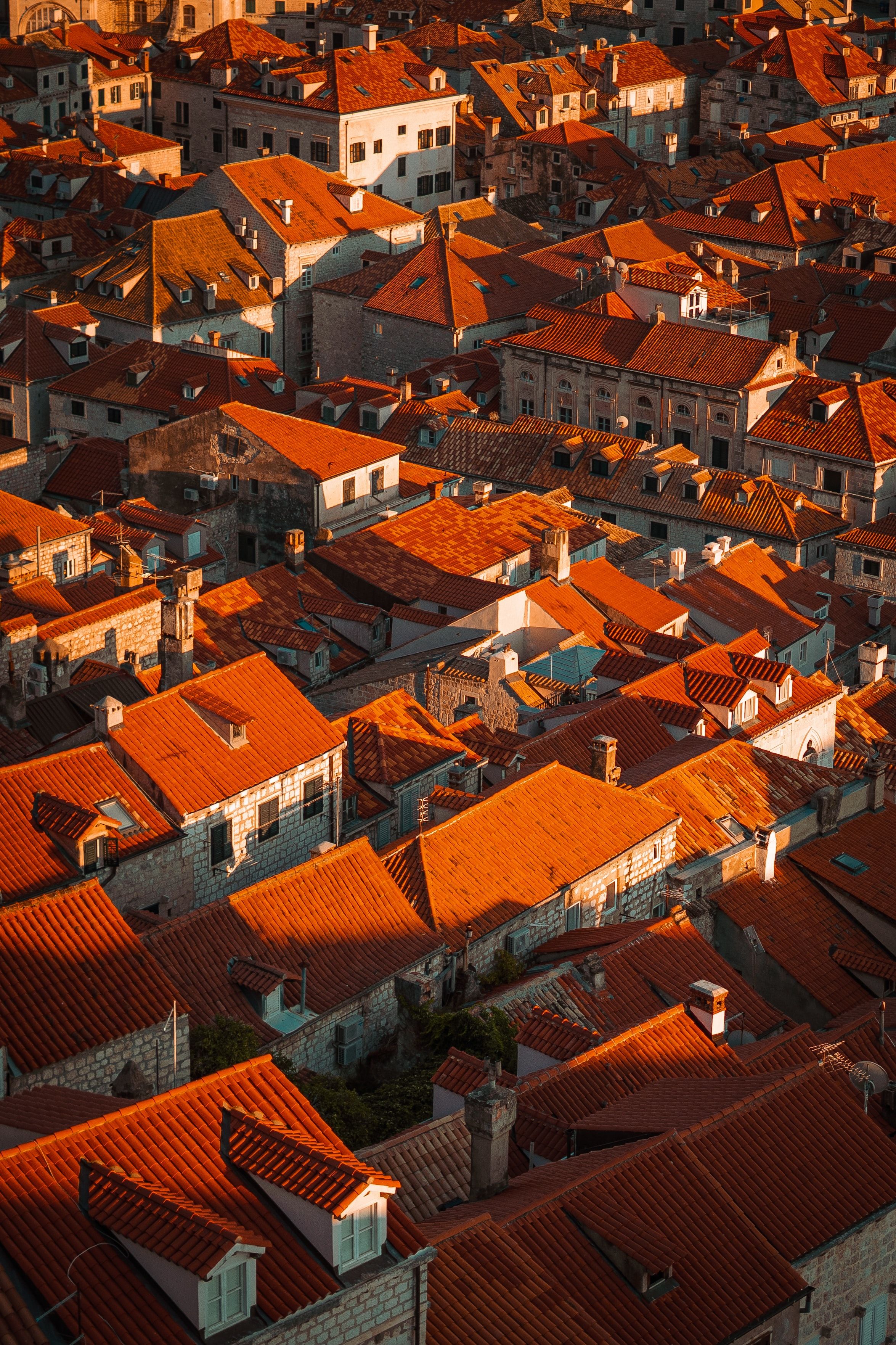 Aerial view of terracotta rooftops in a historic town, bathed in warm sunset light.