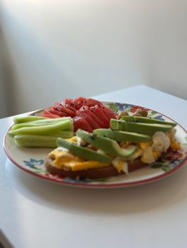 Plate of avocado toast with eggs, watermelon, and cucumber slices, perfect for a nutritious breakfast.