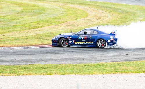 Free A blue racing car drifting on a track, creating a smoke trail under sunny conditions. Stock Photo