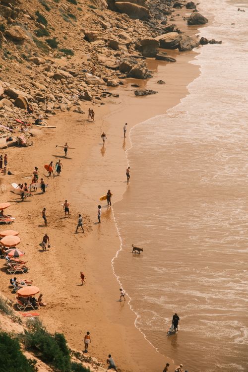 Free People enjoying a sunny day on a rocky beach with umbrellas and waves. Stock Photo