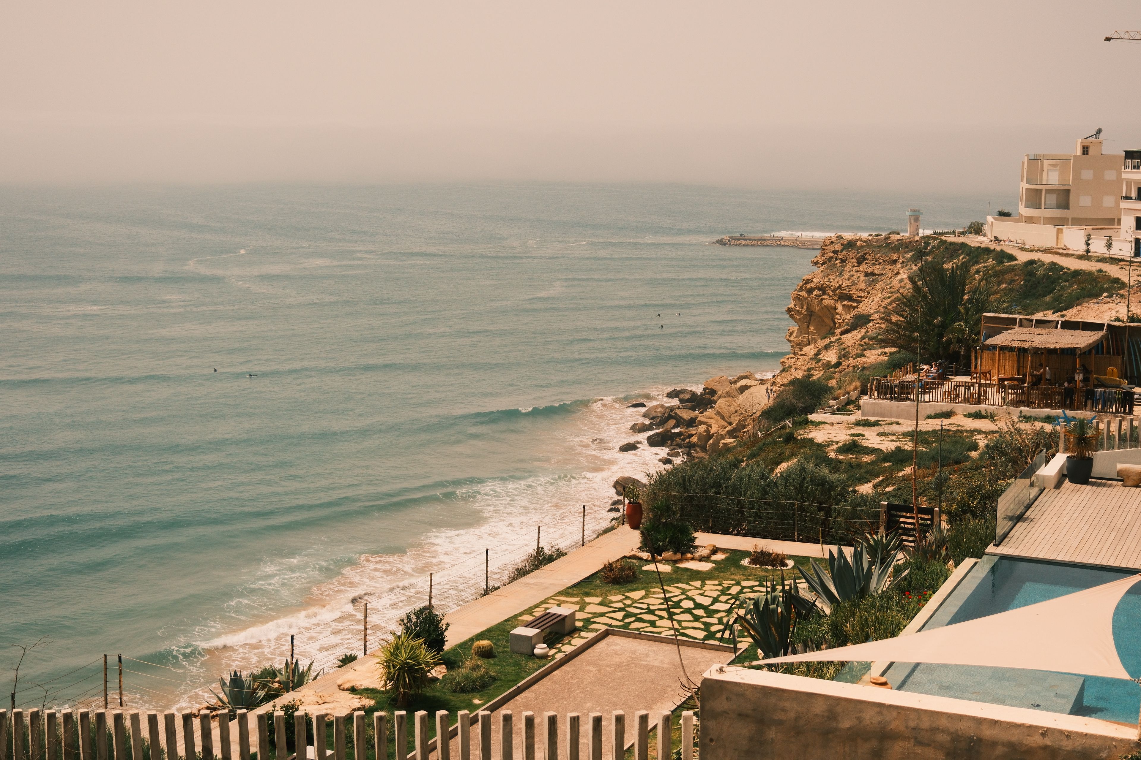 Stunning coastal view of cliffs, ocean, and pool from an elevated angle under a clear sky.
