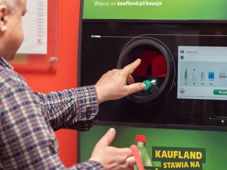 A man inserting a plastic bottle into a return machine at Kaufland in Wrocław, Poland.