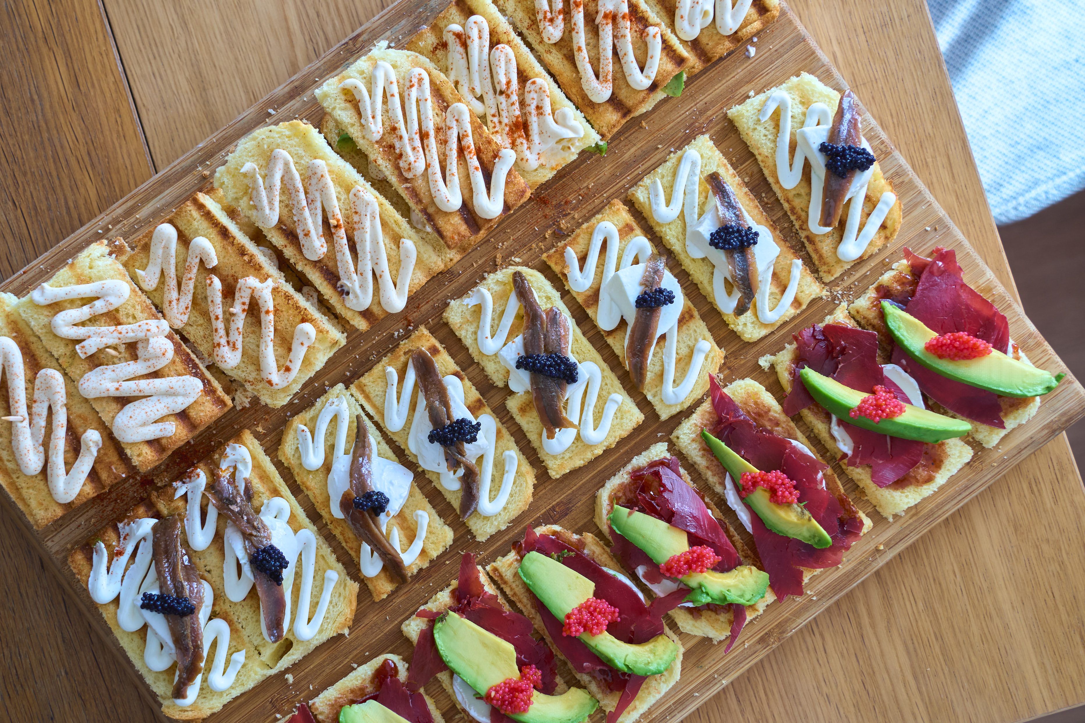 Delightful array of tapas featuring avocado, anchovies, and creamy toppings on a wooden platter.
