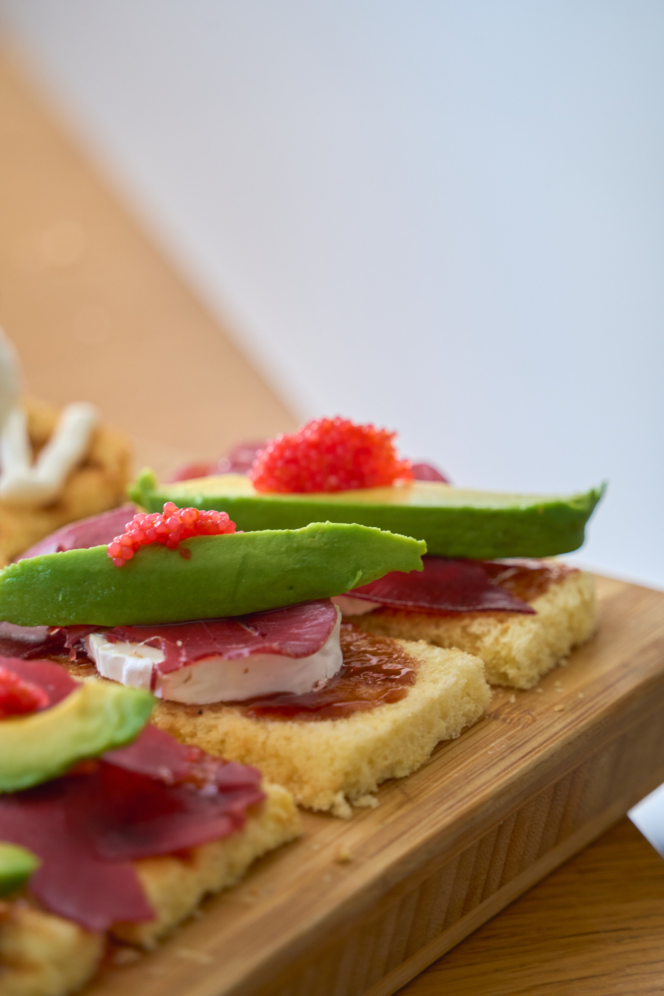 Delicious artisanal avocado toast garnished with cheese, meat, and topping on a wooden board.