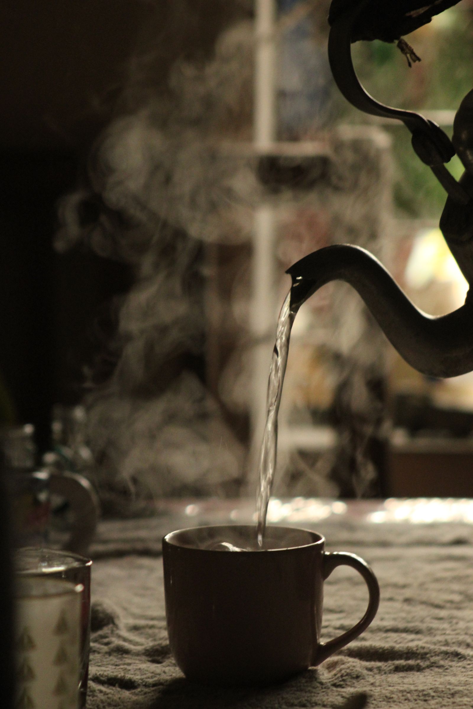 A kettle pouring steaming water into a mug on a cloth-covered table