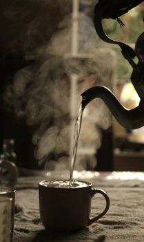 A cozy scene of hot tea being poured from a kettle into a mug, with steam rising.