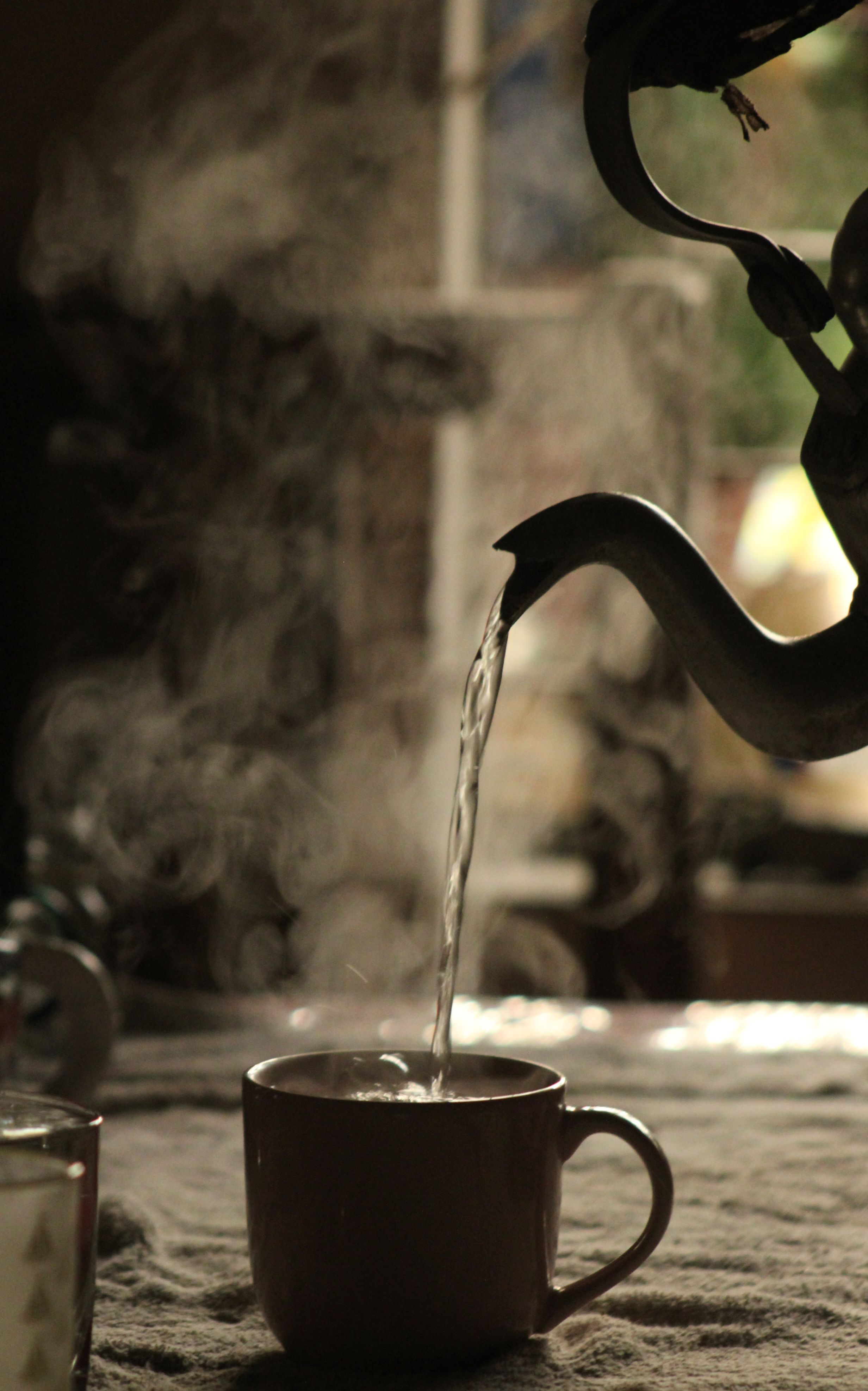 Fotomural Té humeante siendo vertido en una taza desde una tetera en un ambiente interior cálido.