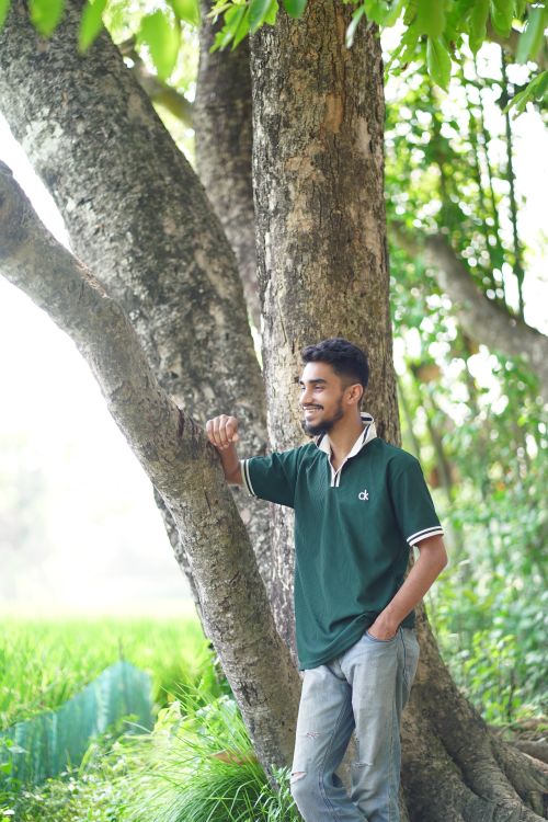 Free Young man standing by a tree in a natural, serene setting, wearing a green polo. Stock Photo