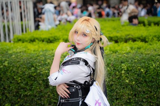 A cosplayer wearing an elaborate costume posing outdoors at an event, surrounded by people.