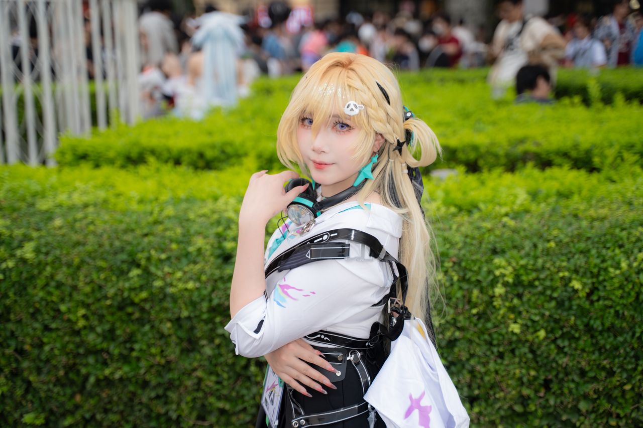 blonde cosplayer poses in costume at an outdoor event with lush green