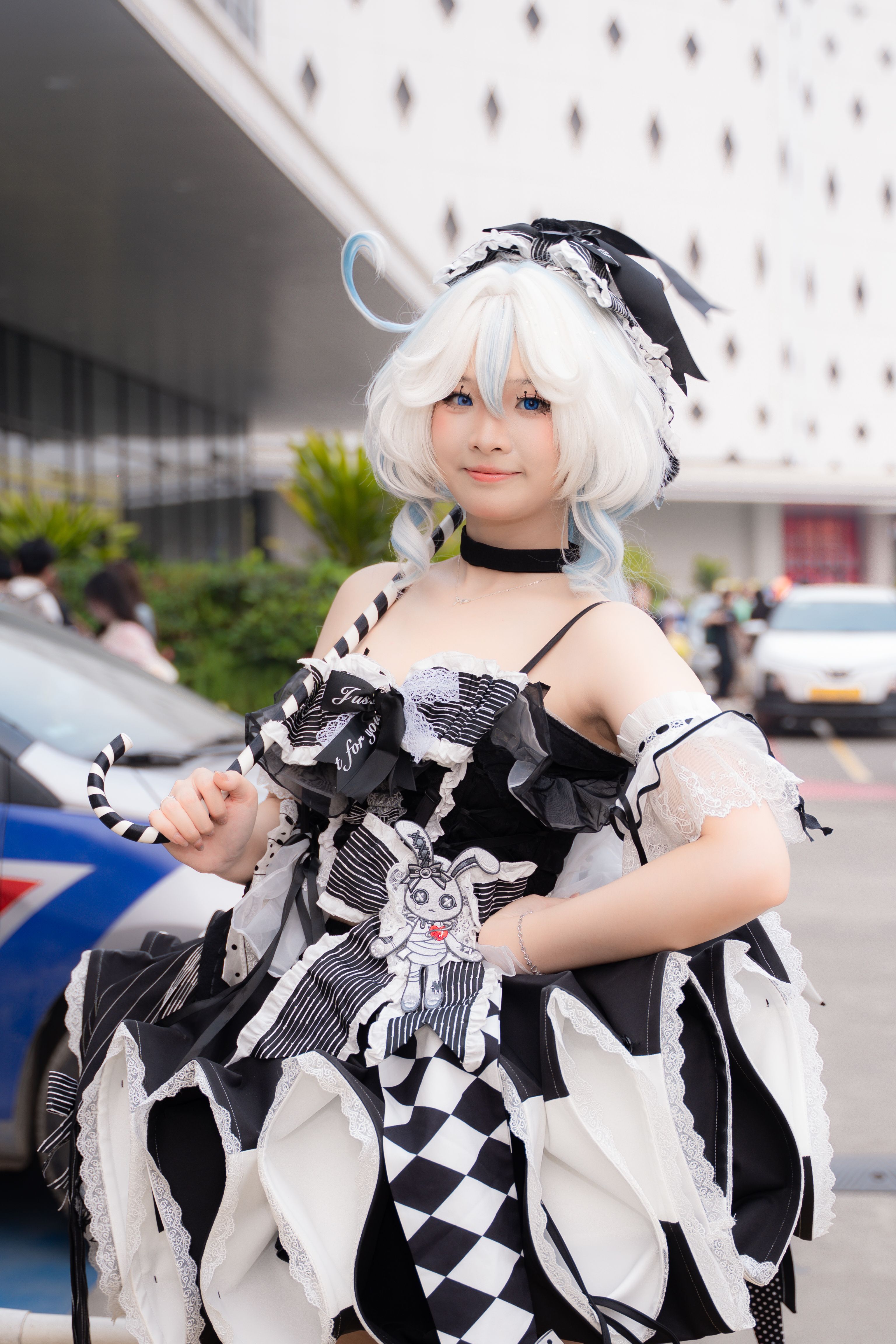 A cosplayer in an elaborate black and white gothic costume posing outdoors.