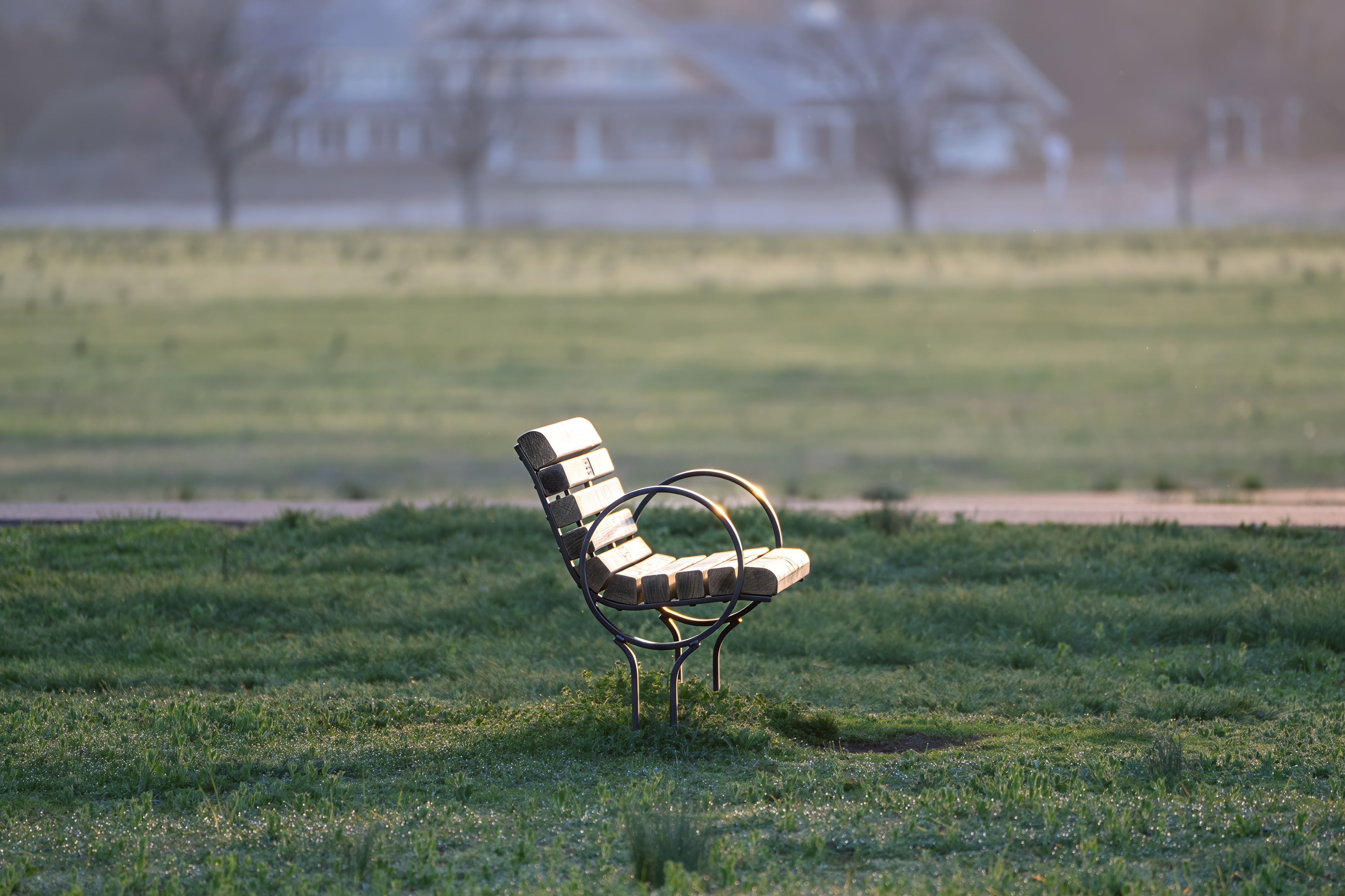 A solitary park bench bathed in soft morning light in an open field, creating a tranquil and peaceful atmosphere.