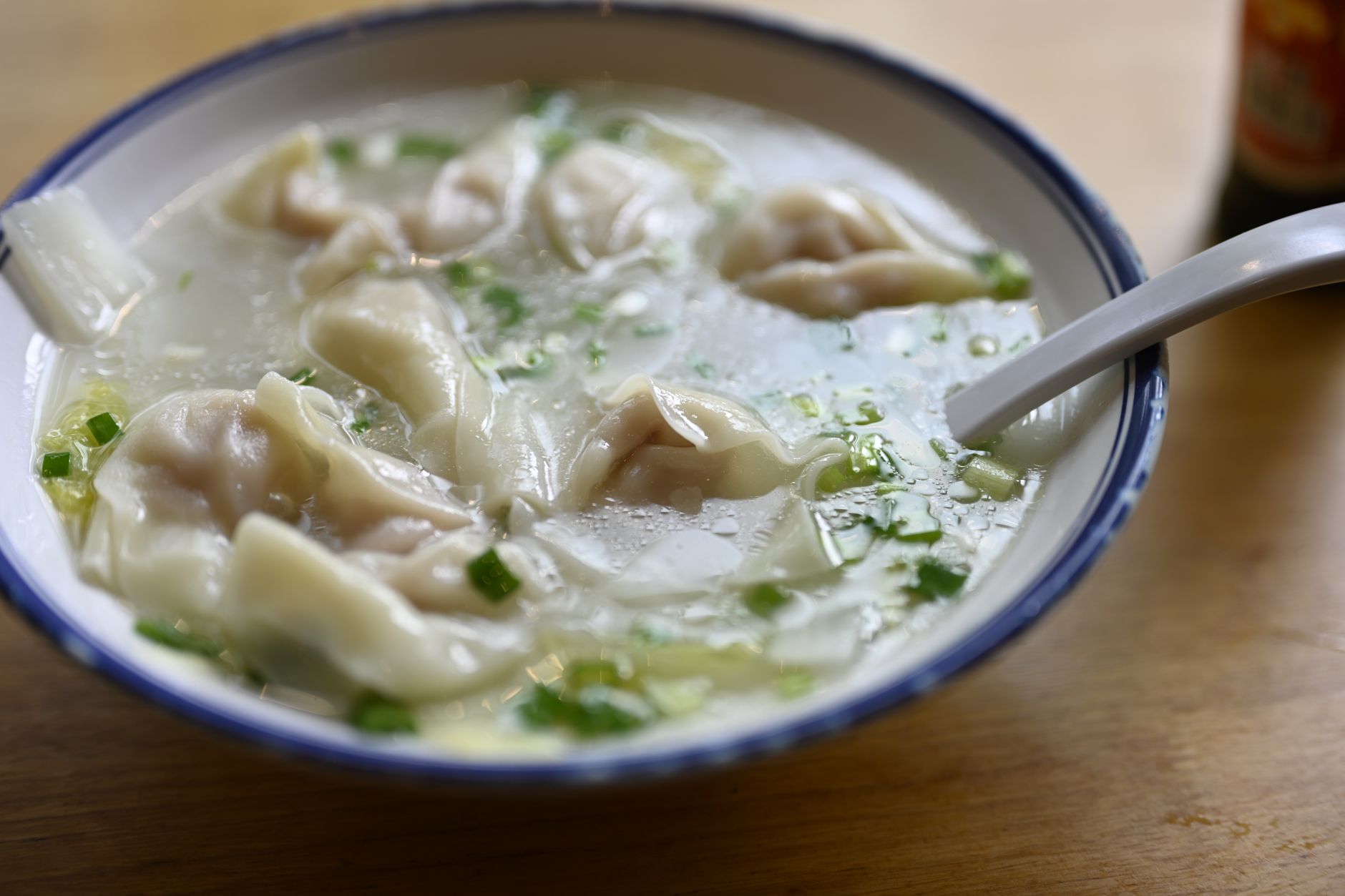 Close-up of tasty wonton soup served in a blue-rimmed ceramic bowl with green onions.