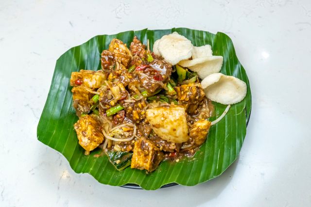 Top view of Indonesian Gado-Gado salad on a banana leaf with spicy peanut sauce and crackers.