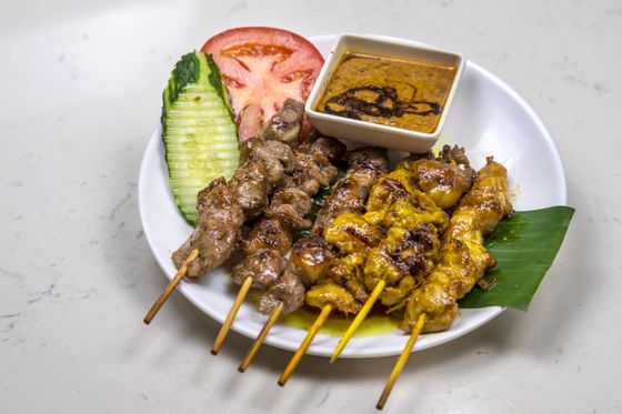 Grilled beef and yellow chicken satay skewers with peanut sauce, cucumber and tomato on banana leaf
