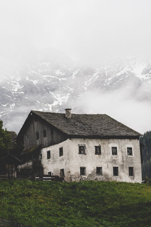 Free A rustic house set against a misty Alpine mountain, showcasing a serene and dramatic nature scene. Stock Photo